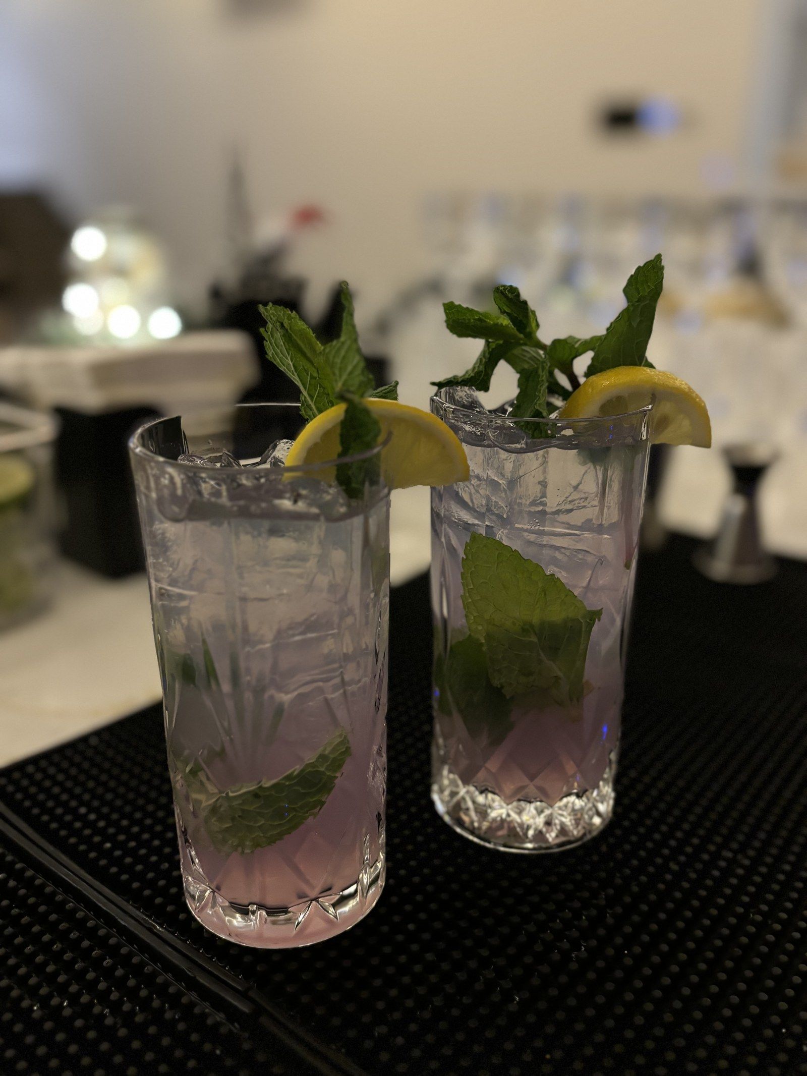 Two lavender highballs with mint and lemon on a bar mat