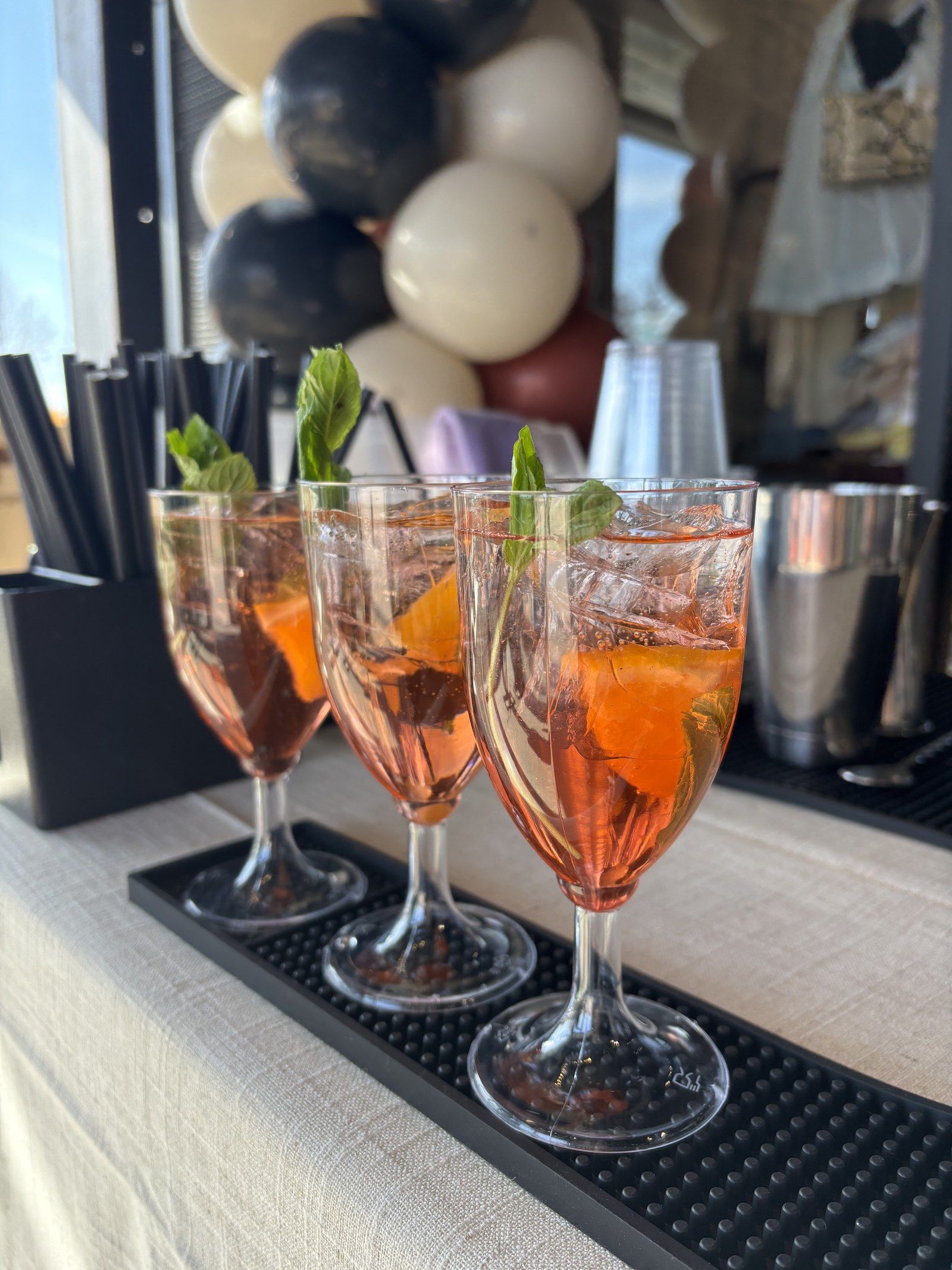 Three orange spritzes with mint lined up on the bar in front of a balloon garland